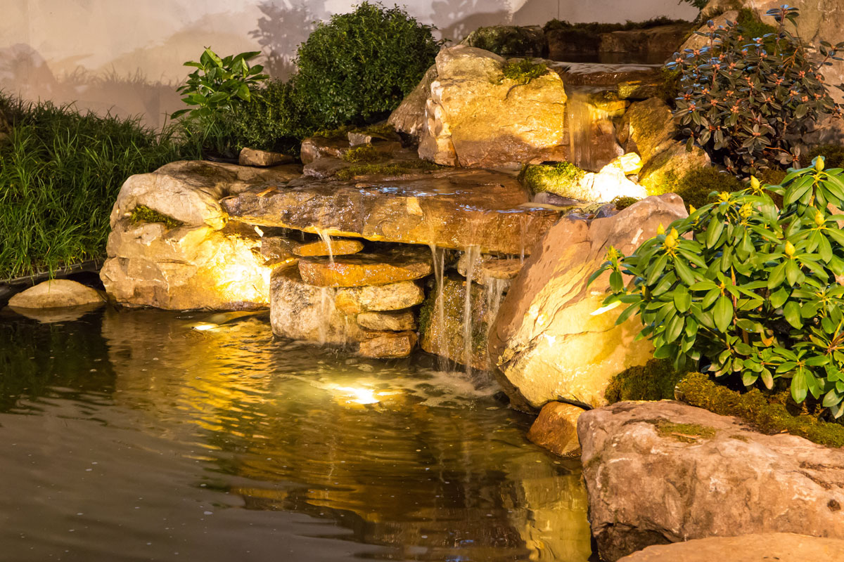 Brightly Lit Waterfall and Pond. D & F Plumbing in Portland OR and Vancouver WA offers tips for adding a backyard water feature to your property.