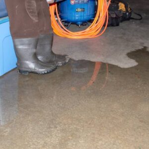 Person in rubber boots standing next to a puddle on the basement floor
