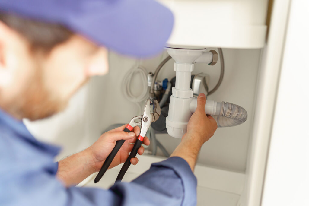 Close up of professional plumber installs a siphon pipe on the kitchen sink