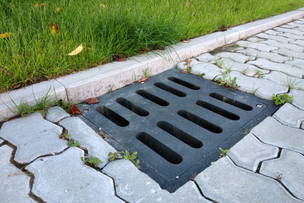 Plastic drain gutter, green grass lawn and stone pavement sidewa