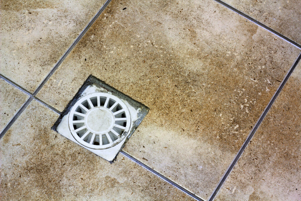 Water drain vent in kitchen, bathroom or basement ceramic tiled old vintage floor. Geometric abstract beige background.