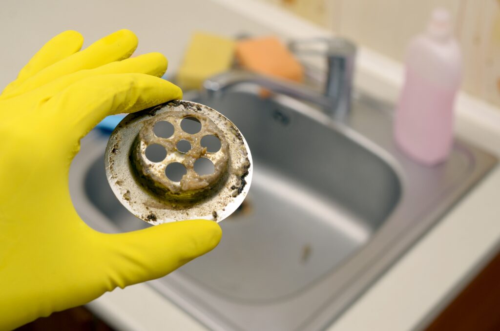 Cleaner in rubber gloves shows waste in the plughole protector of a kitchen sink