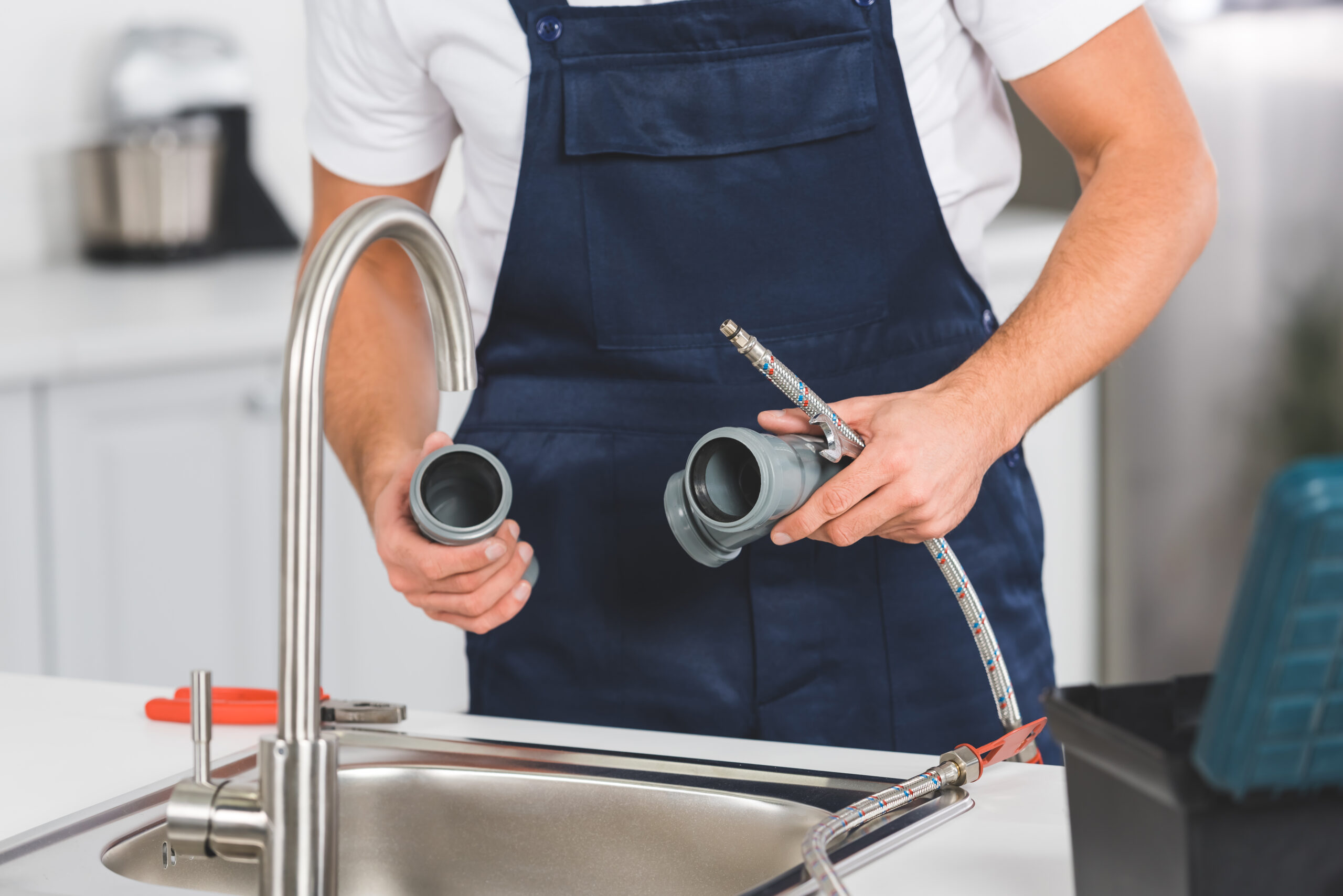 cropped view of repairman holding pipes and tools while repairing faucet at kitchen