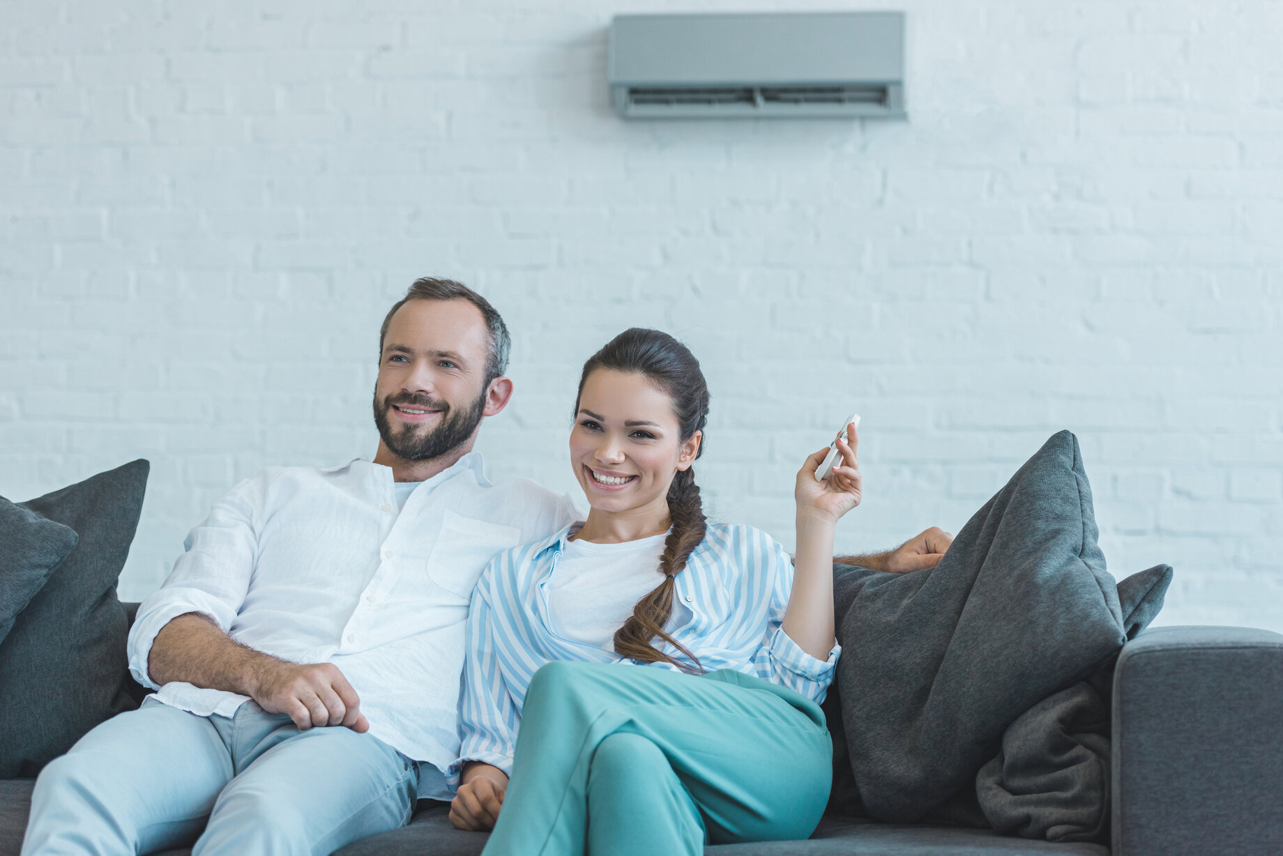 happy couple turning on air conditioner with remote control during the summer heat at home