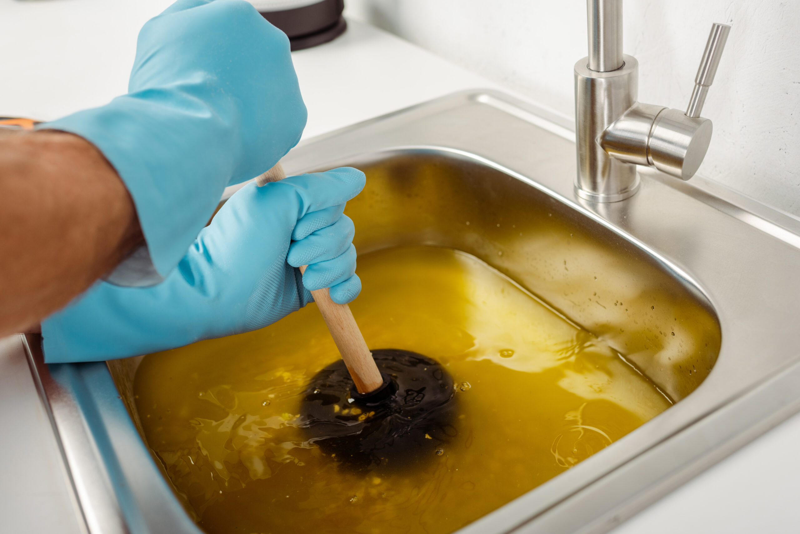 Cropped view of plumber in rubber gloves holding plunger while cleaning blockage of kitchen sink